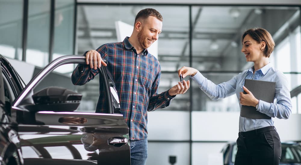 A salesperson is shown handing a set of car keys in a dealership.