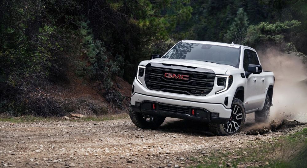 A white 2024 GMC Sierra for sale in Corinth is shown driving off-road.