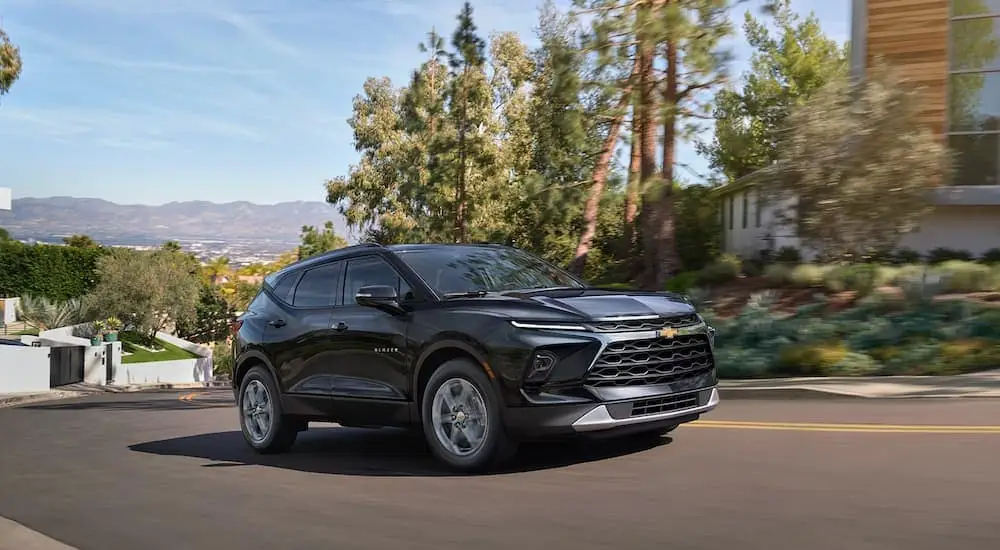 A black 2025 Chevy Blazer is driving on a winding city street.