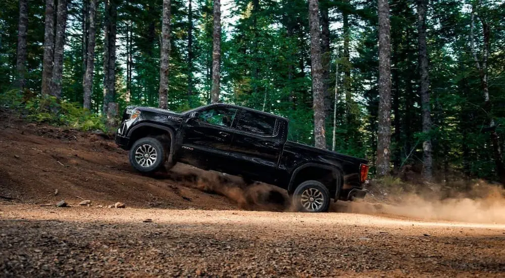 A black used 2020 GMC Sierra 1500 AT4 for sale is shown from the side driving on a dirt road.