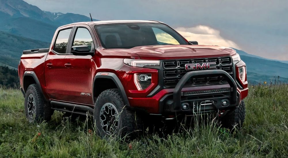 A red 2025 GMC Canyon AT4X parked offroad on a grassy hillside.