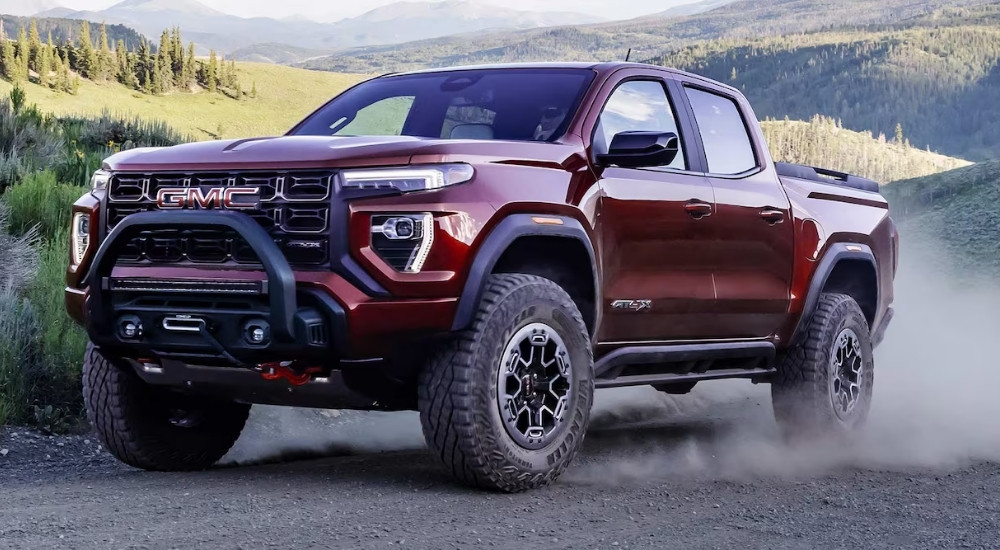 A red 2025 GMC Canyon AT4X is shown kicking up dust on a trail.