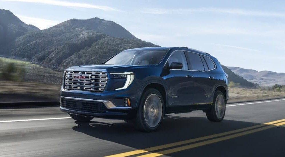 A blue 2025 GMC Acadia for sale driving on a highway.