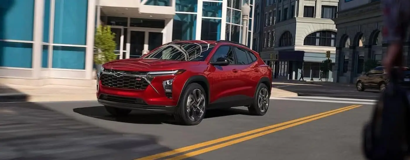 A red 2024 Chevy Trax RS is shown driving on a city street.