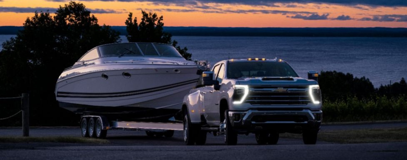 White 2025 Chevy Silverado 3500 HD towing a boat at dusk