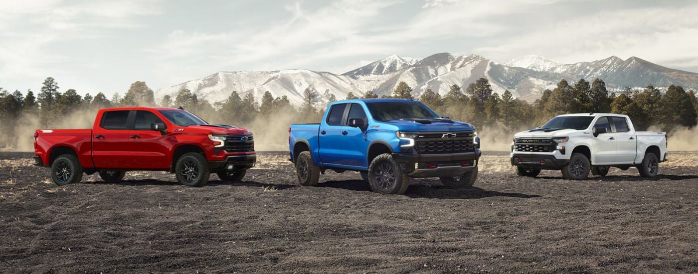 A trio of Chevy Silverado 1500s in red, blue and white parked in front of a mountain range.