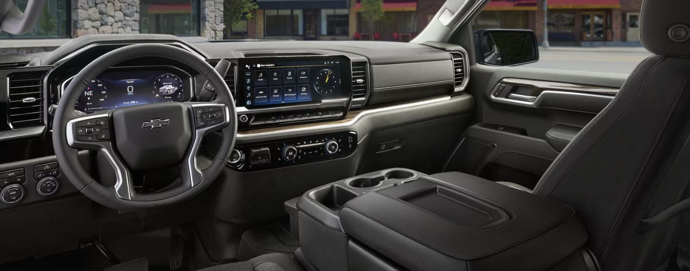 The black front interior of a 2026 Chevy Silverado 1500 showing steering wheel and infotainment display.