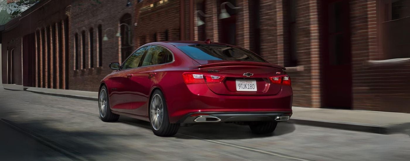 A red 2022 Chevy Malibu is shown from a rear angle driving down a city side street.
