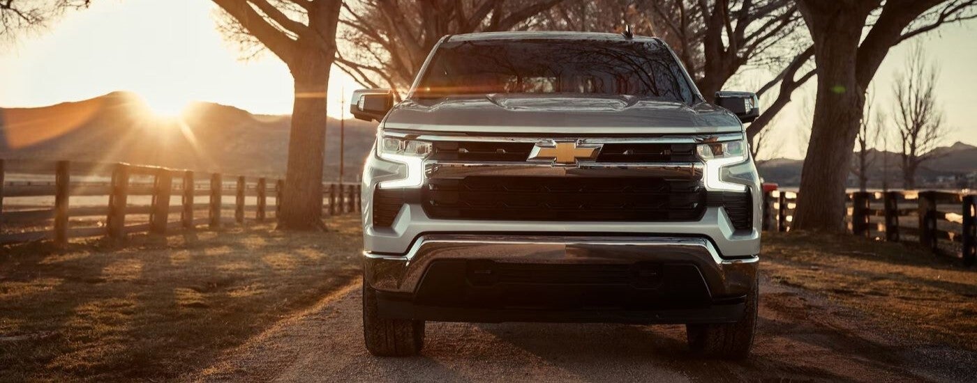 Front angle view of a silver 2024 Chevy Silverado 1500 High Country driving on a dirt trail.
