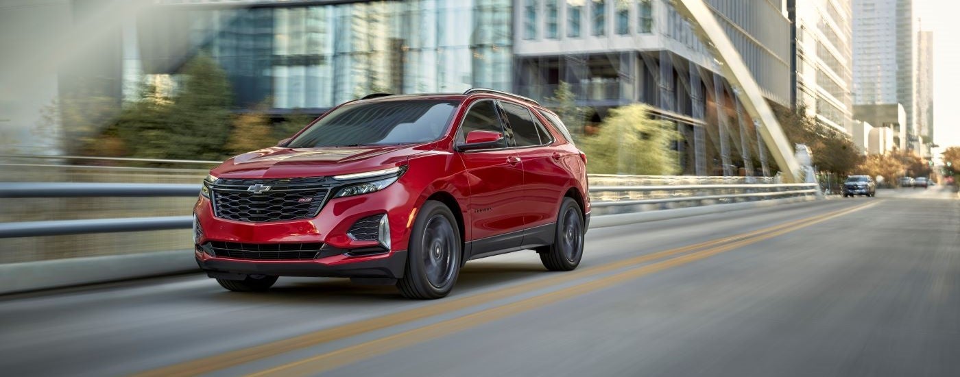 Red 2025 Chevy Equinox RS for sale driving through a city.