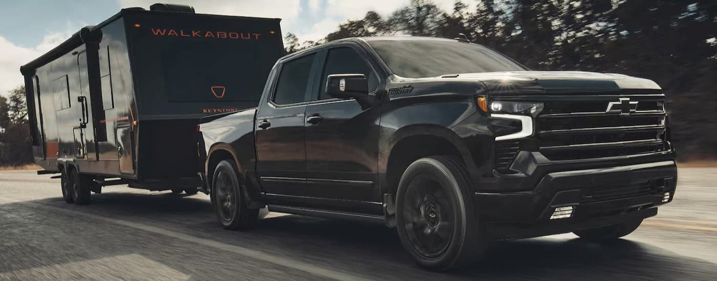 Black 2026 Chevy Silverado 1500 towing a trailer on a highway.
