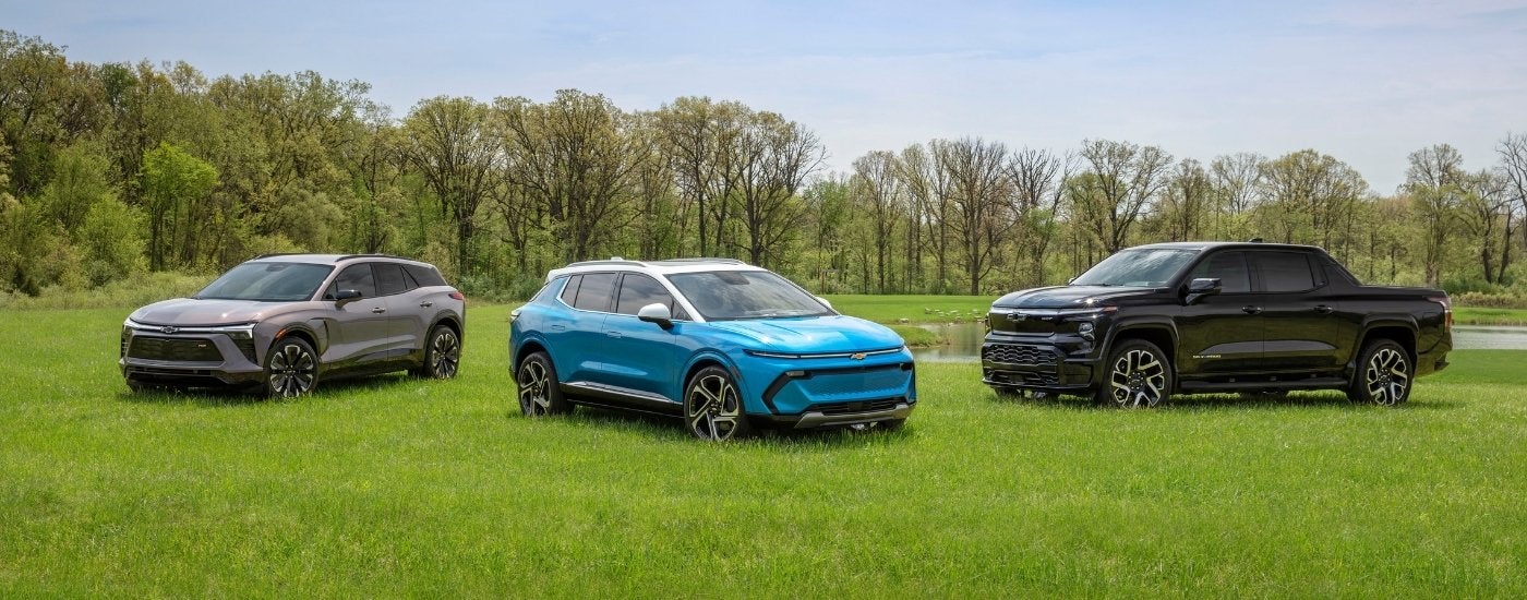 A grey 2024 Chevy Blazer EV RS, a blue Equinox EV, and a black Silverado EV RST are shown parked on grass.