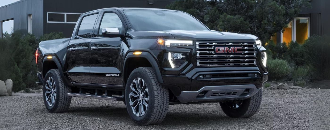 A black 2024 GMC Canyon Denali parked in a gravel driveway.