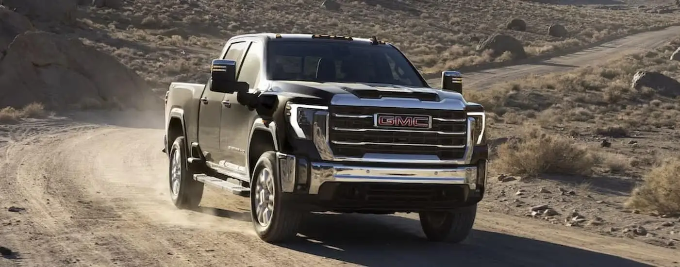 A black 2024 GMC Sierra 2500 HD is shown driving on a dirt road.