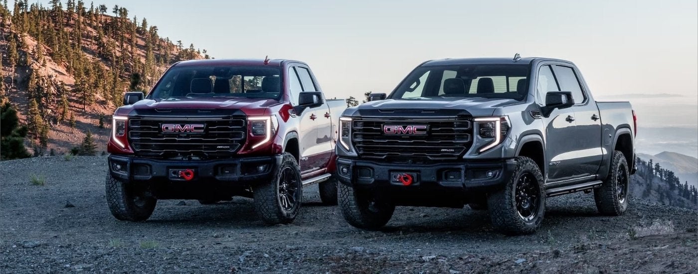 A red 2024 GMC Sierra 1500 AT4X and grey AT4X AEV are shown parked at an overlook.
