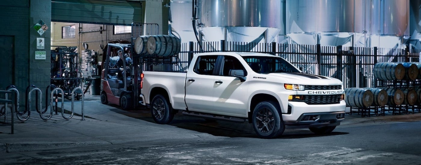 A white 2021 Chevy Silverado 1500 is shown being loaded with barrels.
