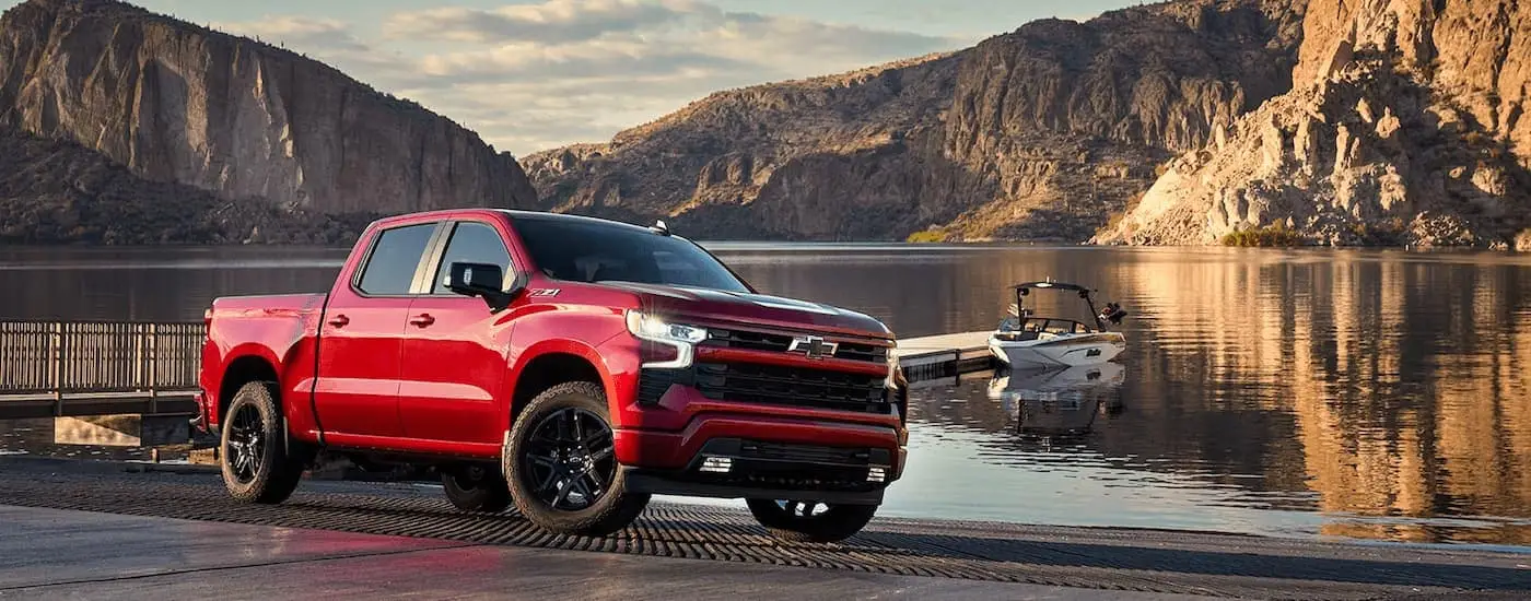 A red 2023 Chevy Silverado 1500 LTZ Z71 is shown parked at a boat launch next to a lake.