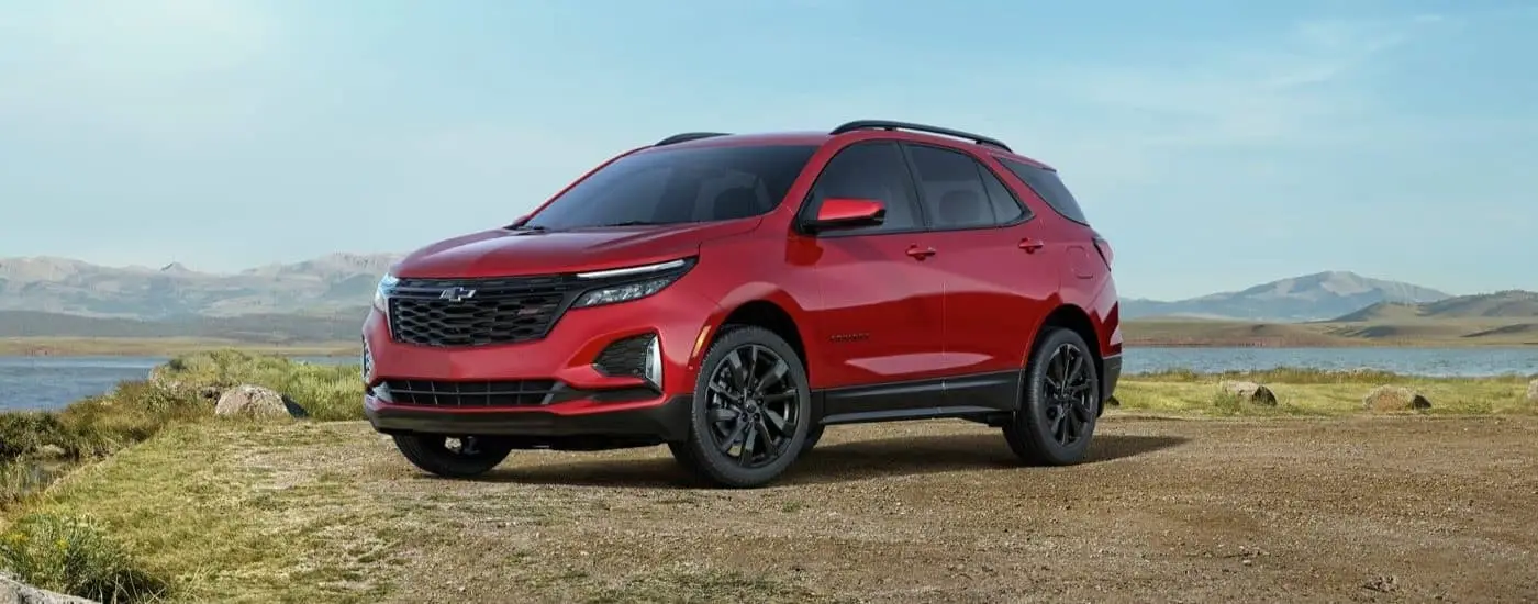 A red 2024 Chevy Equinox RS is shown angled left and parked on a grassy hill.