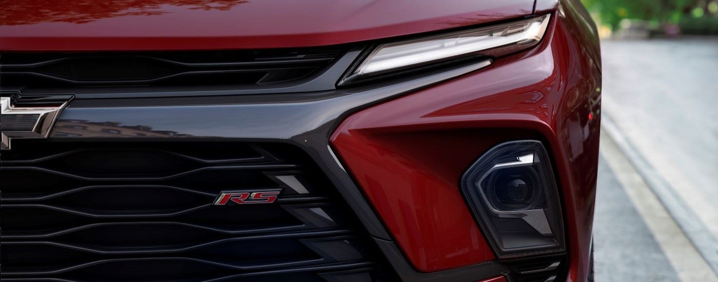 A close-up of the driver-side grille and headlight on a red 2023 Chevy Blazer RS are shown.