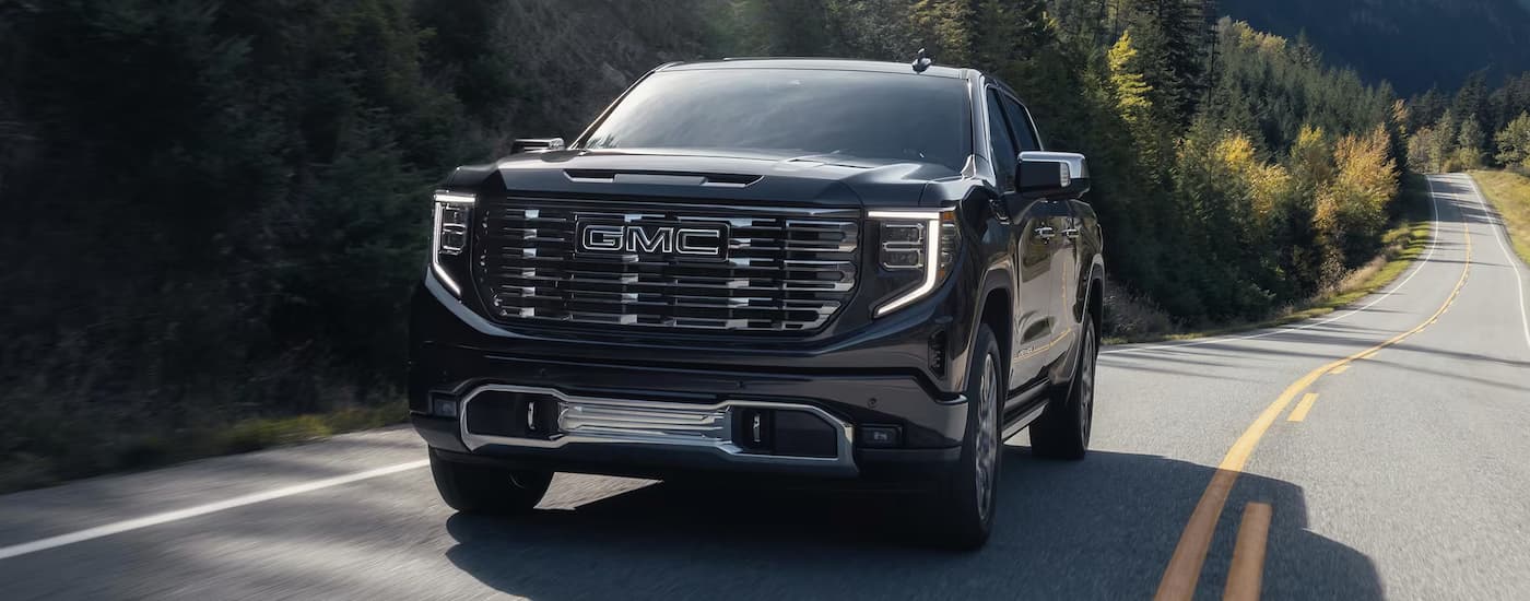 A black 2025 GMC Sierra 1500 Denali Ultimate driving down a winding road from a dealer with a Sierra 1500 for sale in Corinth.