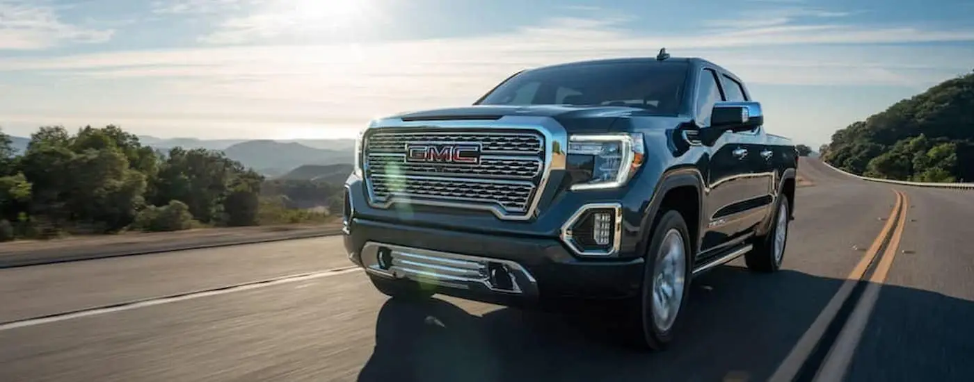A grey used 2020 GMC Sierra 1500 for sale is driving on an open highway with trees in the background.