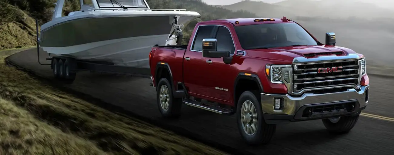A red used GMC truck, a 2020 GMC Sierra 2500, is shown towing a small boat on a winding road.
