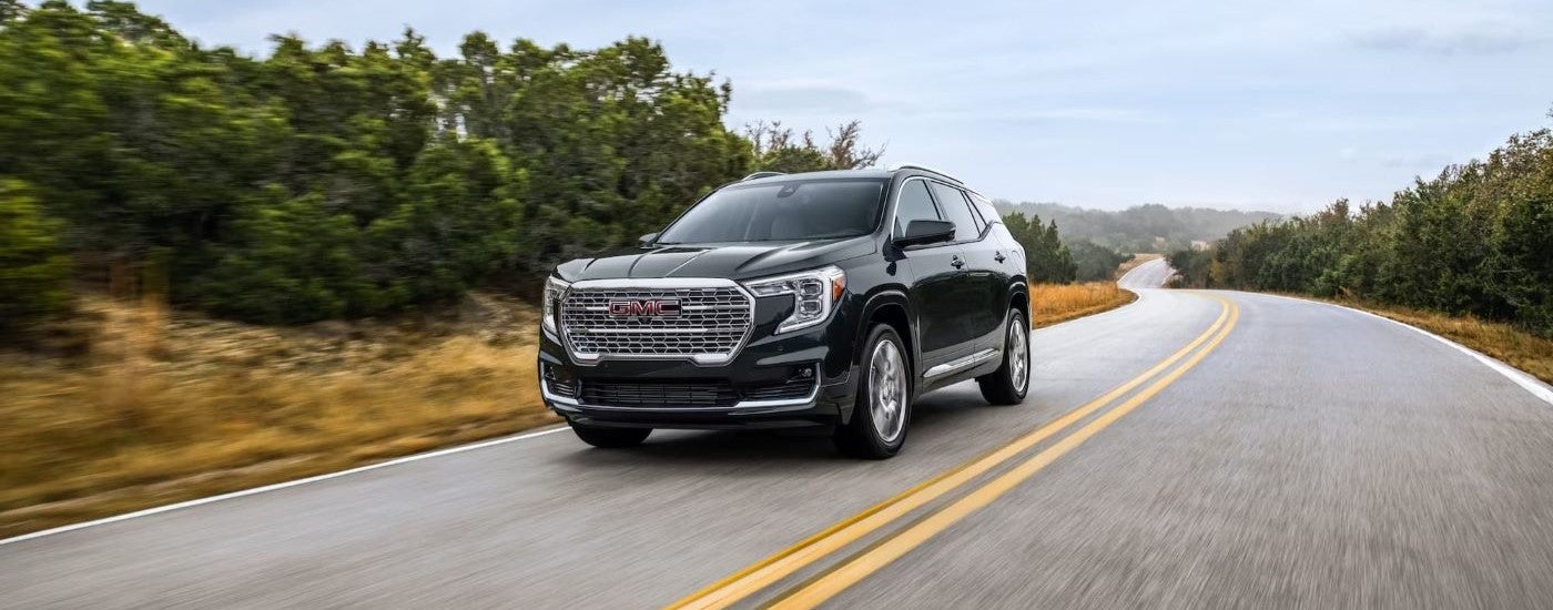 A black 2023 GMC Terrain Denali is shown driving on a highway.