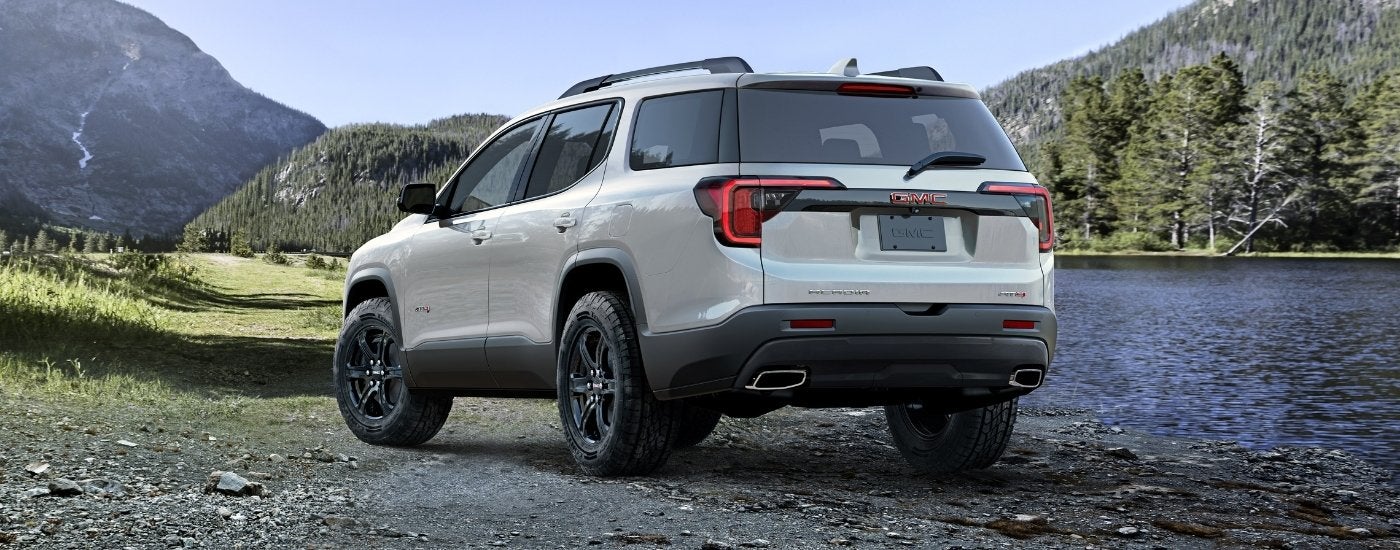 A white 2023 GMC Acadia AT4 is shown near a lake.