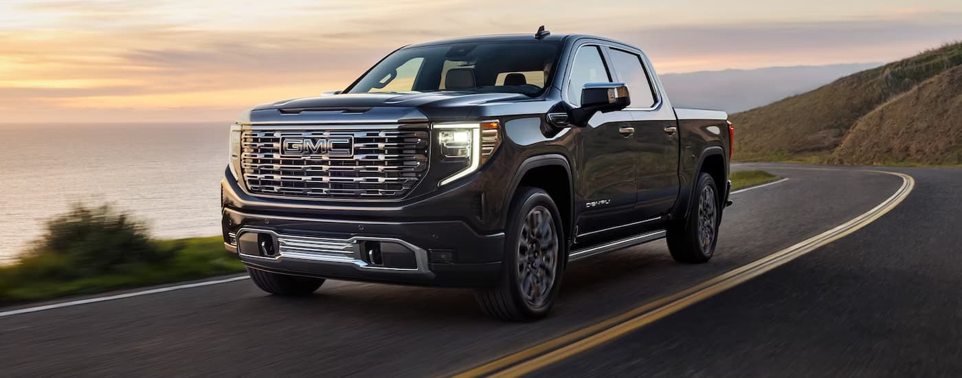 A black 2022 GMC Sierra 1500 Denali Ultimate is shown driving on an open road after leaving a used GMC dealer.