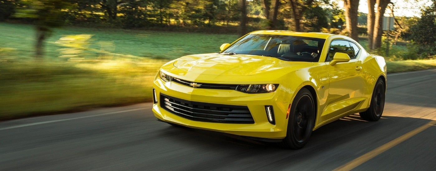 A yellow 2018 Chevy Camaro driving down a tree lined road.