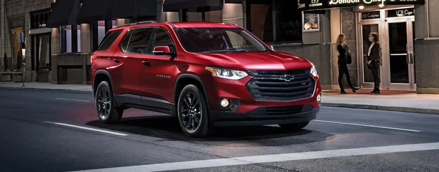 A red 2020 Chevy Traverse RS driving from a dealer with used SUVs for sale.
